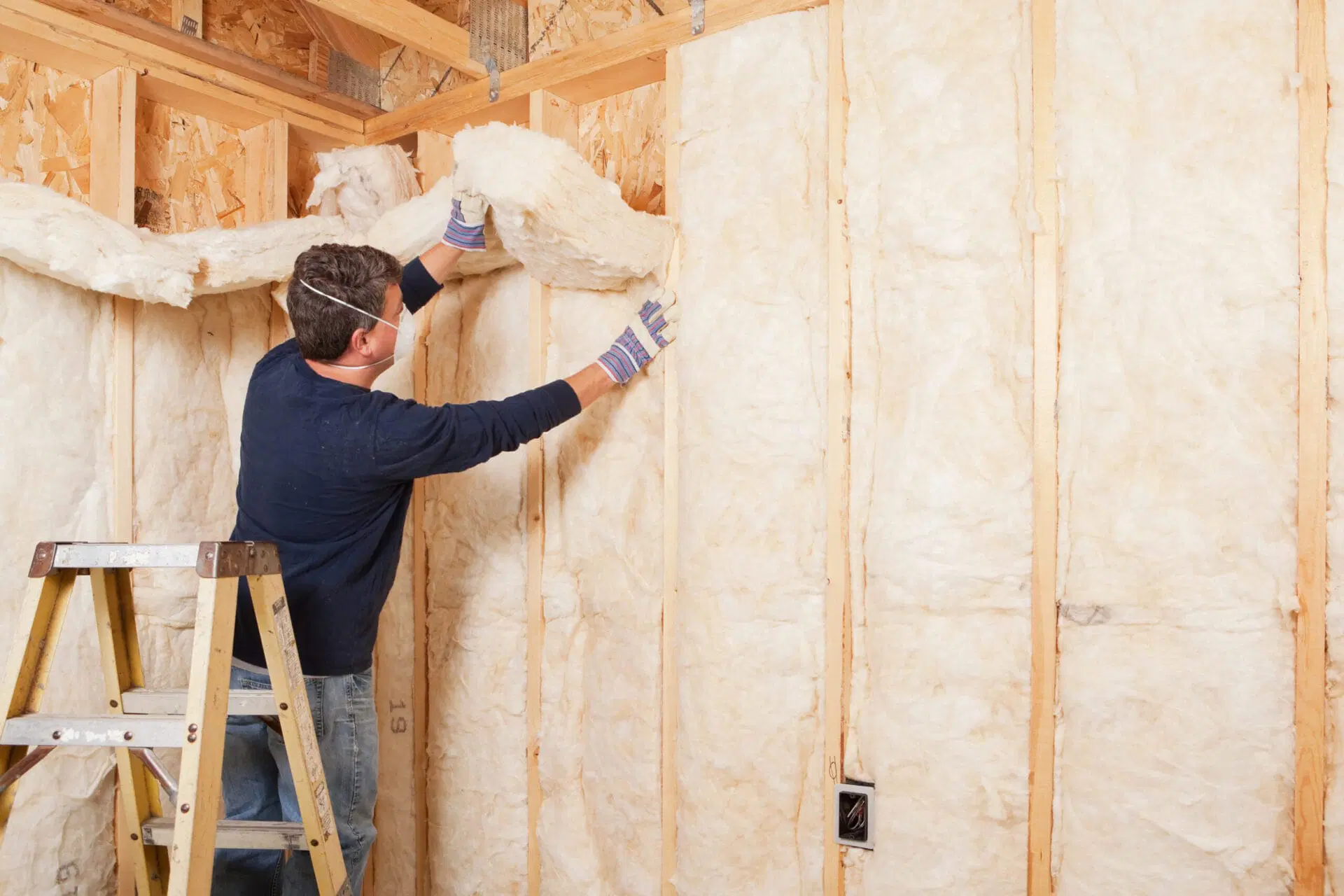 Installer fitting thermal insulation batts between timber wall studs
