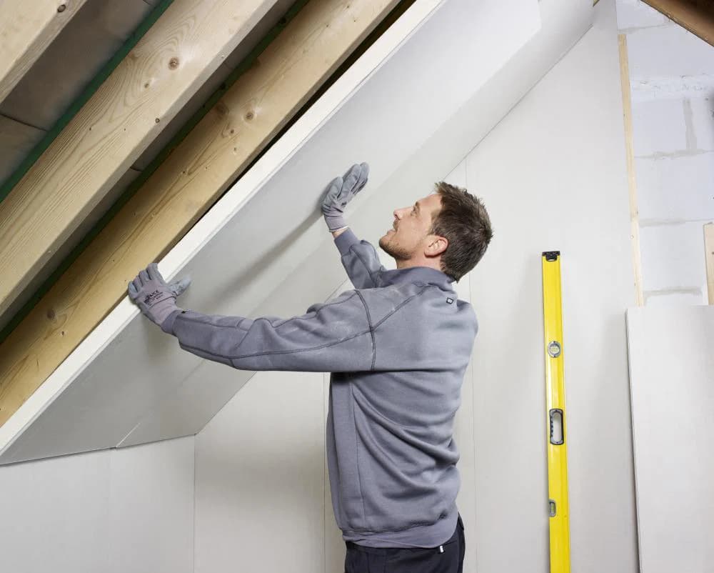 Tradesperson fitting plasterboard to a raked attic wall