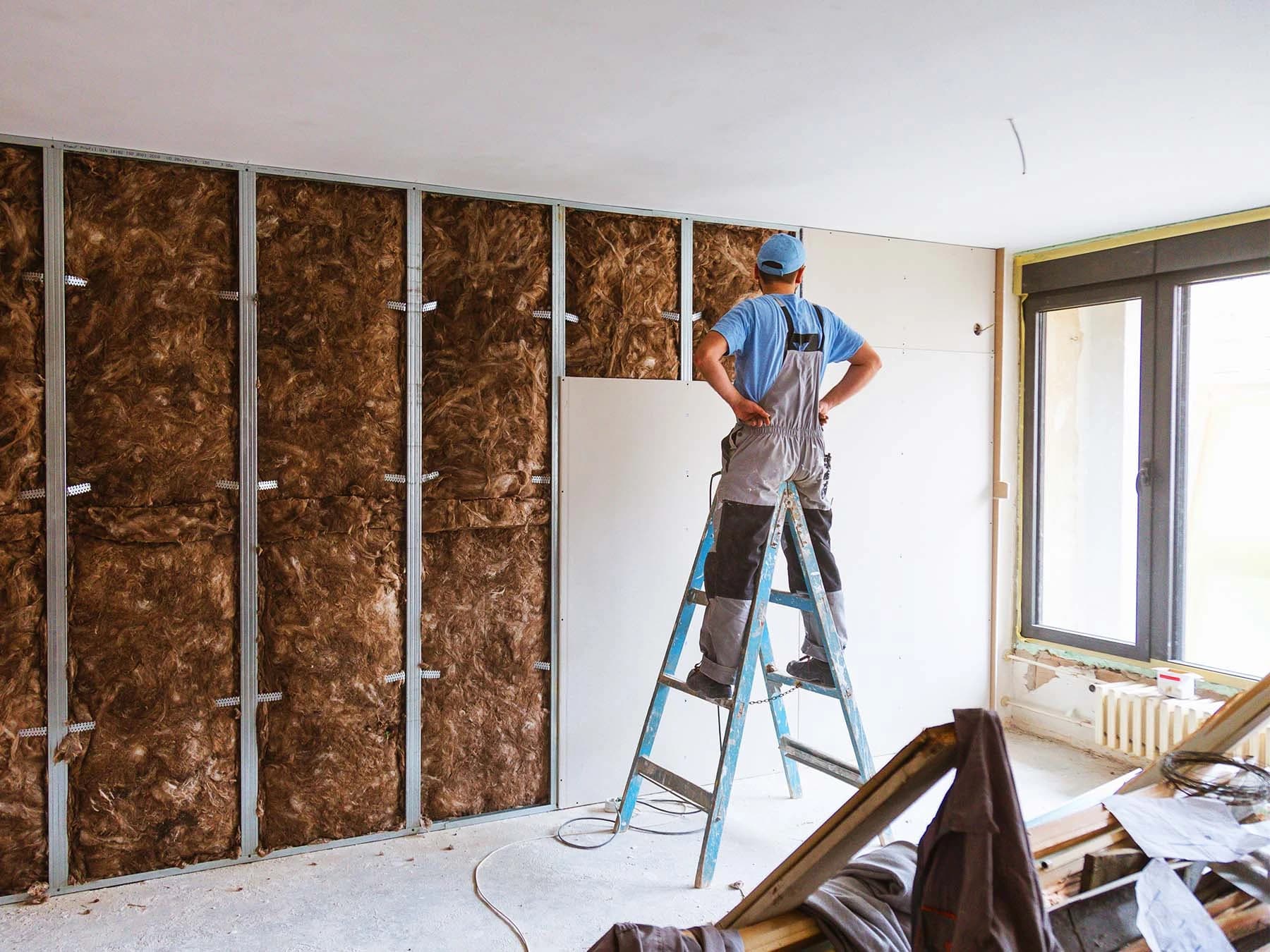 Plasterboard fixer installing wall sheets over an insulated steel stud frame