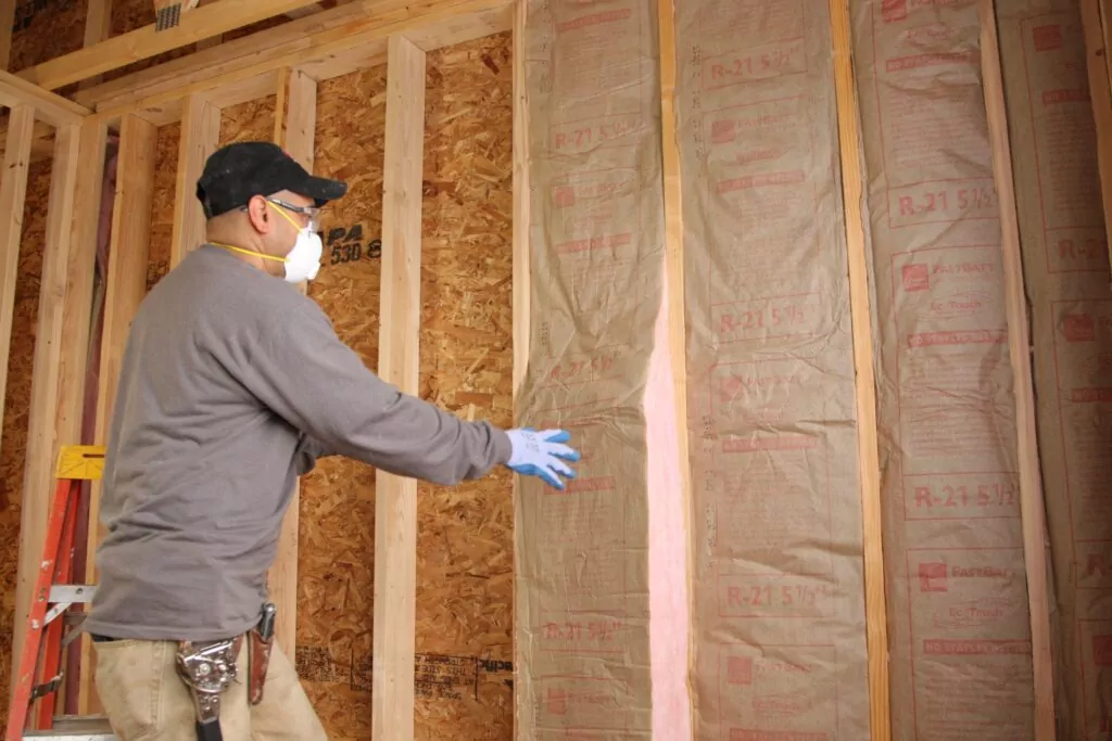 Installer fitting high R-value faced insulation batts in an external wall